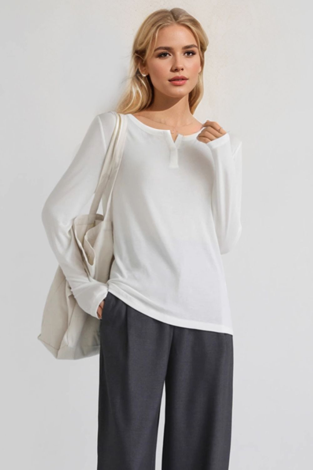 Woman wearing Basic Bae Notched Long Sleeve T-Shirt with a notched neckline, styled with dark pants and a white bag.