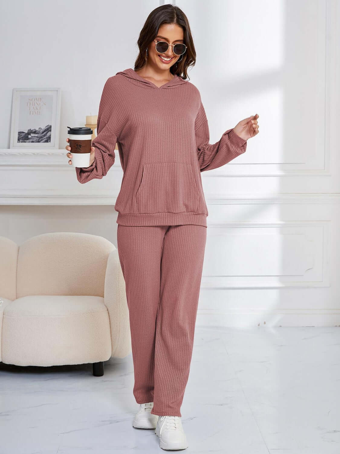 Woman in dusty pink Bella Road hoodie and pants set, holding coffee cup, stylish and cozy lounge wear.