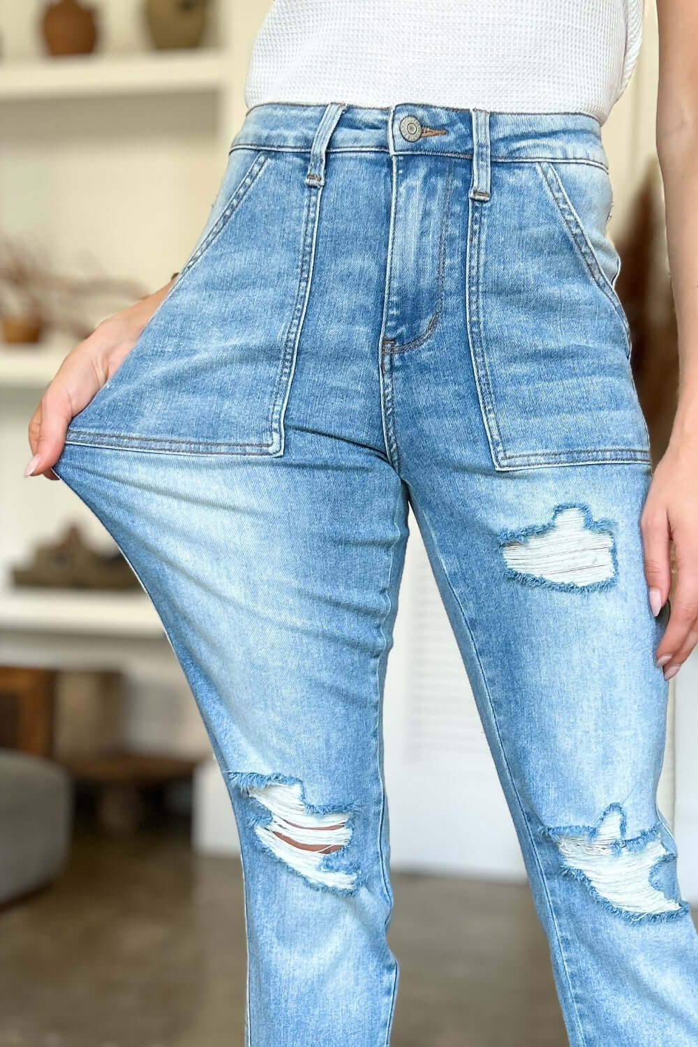 Woman wearing Judy Blue distressed straight jeans with high waist and patch pockets, highlighting trendy ripped details and flattering silhouette.