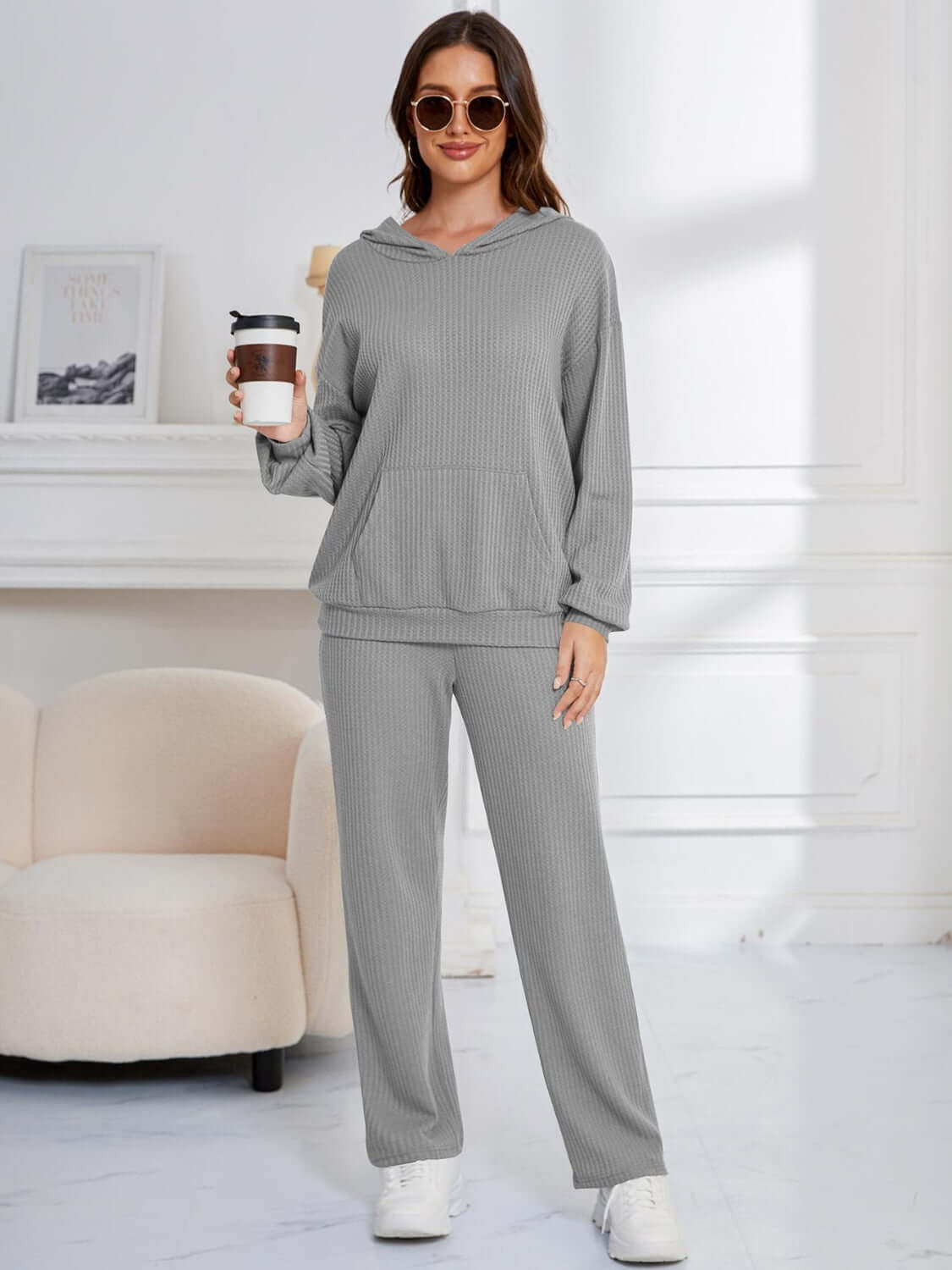 Woman in gray Bella Road hoodie and pants set holding coffee, showcasing cozy and stylish loungewear in a relaxed fit.