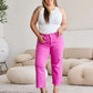 Woman in white tank top and pink high-waisted jeans standing in stylish living room.