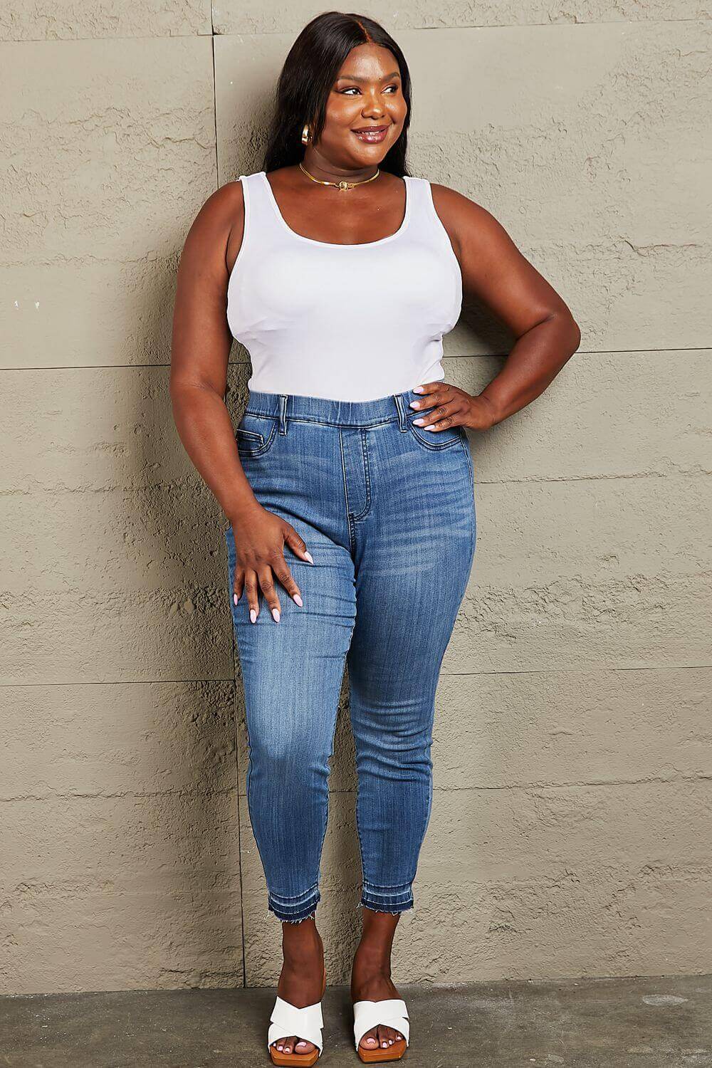 Woman wearing Janavie Full Size High Waisted Pull On Skinny Jeans with a white tank top, showcasing the premium stretch denim and release hem detailing.