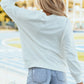 Woman wearing Bella Road Game Day Round Neck Long Sleeve Sweatshirt in white, standing near a sports stadium