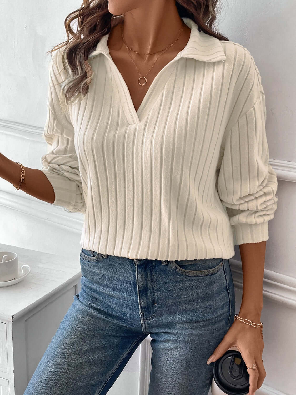 Woman wearing a white ribbed Johnny collar long sleeve t-shirt with blue jeans, holding a coffee cup.