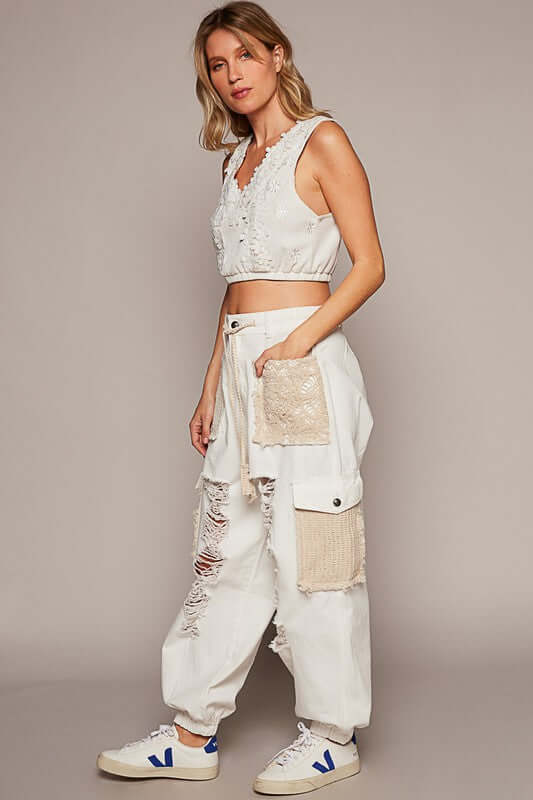 Stylish model in distressed white jeans with crochet patches, paired with a matching crop top and trendy sneakers.