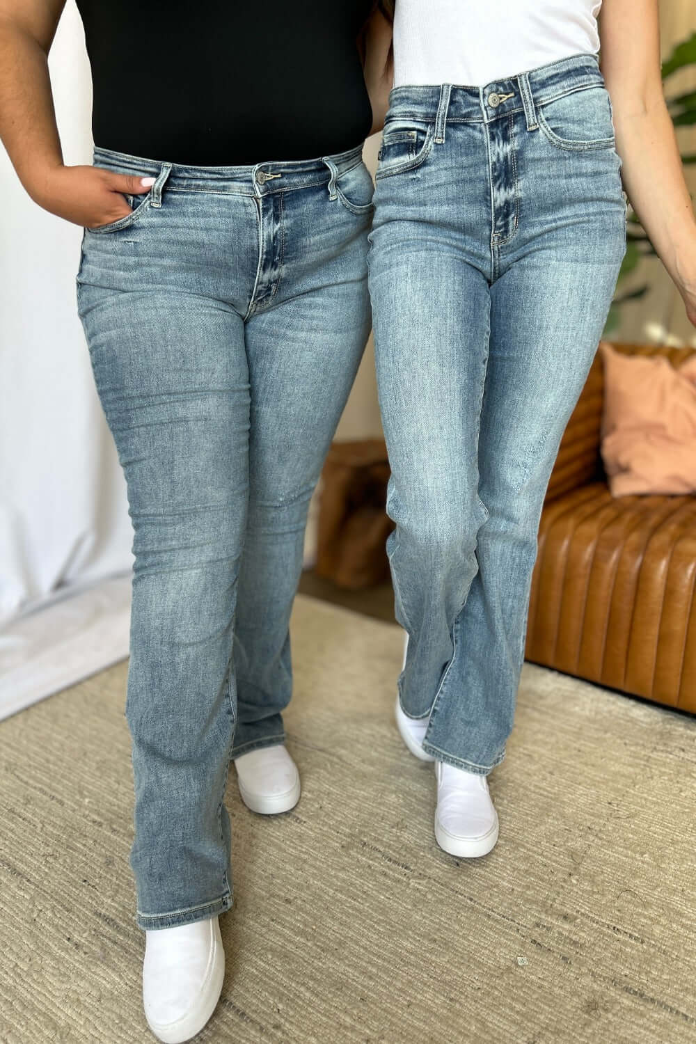 Two women wearing Judy Blue Full Size Medium Rise Bootcut Jeans in light blue denim, showcasing the comfortable fit and slight flare.