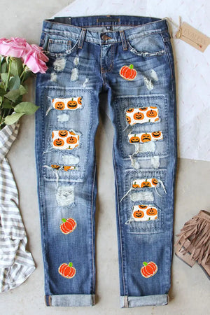 Distressed pumpkin jeans with pockets, featuring Halloween-themed patches and a slightly stretchy fit, laid flat with pink flowers and accessories.