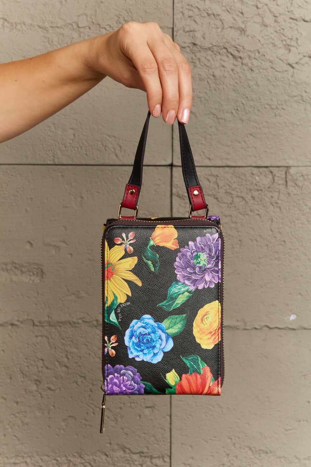 Hand holding Nicole Lee USA small crossbody wallet with colorful floral pattern, featuring removable strap and multiple compartments.