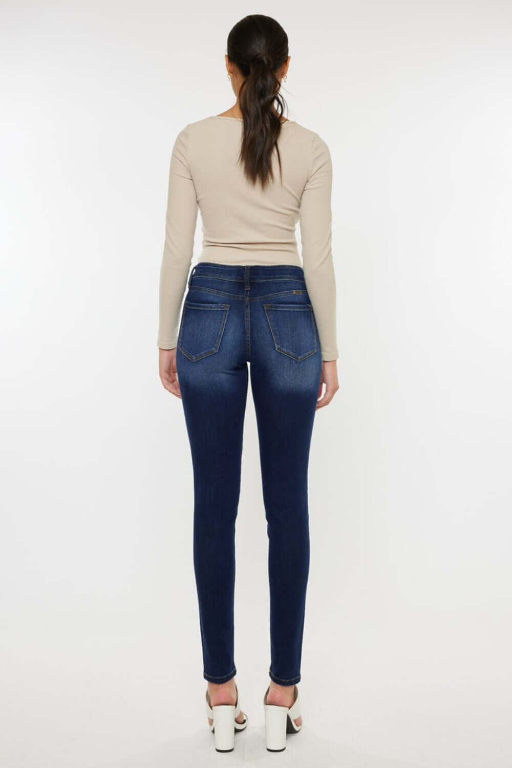 Back view of woman wearing mid rise gradient skinny jeans with a beige top and white heels.