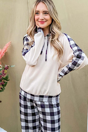 Woman smiling in a cozy drawstring hooded top and plaid pants lounge set, showcasing relaxed chic style.