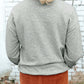 Back view of woman wearing Bella Road Game Day Round Neck Long Sleeve Sweatshirt with orange pants against a white brick wall.