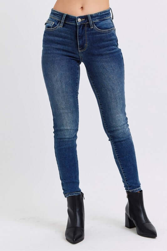 Judy Blue mid-rise waist skinny jeans in dark wash, featuring pockets, styled with chic black heeled boots.