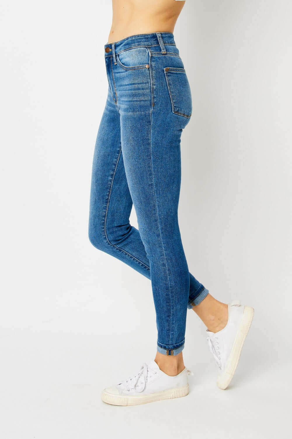 Woman wearing cuffed hem low waist skinny jeans from Judy Blue, showcasing a sleek slim fit and modern design paired with white sneakers.