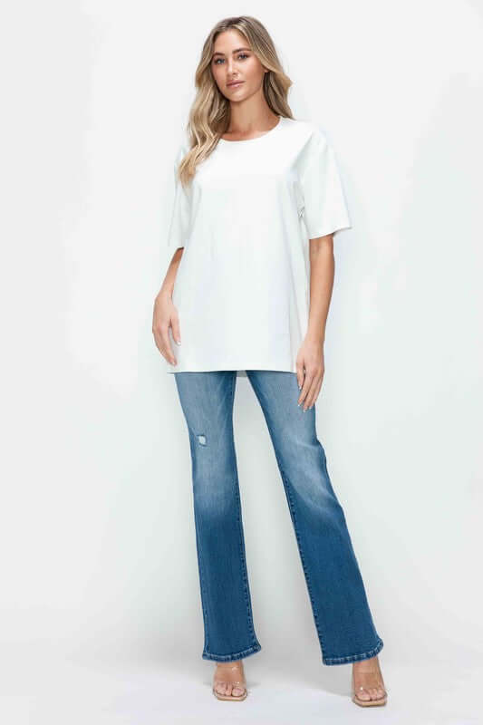 Woman in a white oversized shirt and distressed high rise jeans with pockets, showcasing modern vintage style.