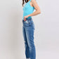 Model wearing Judy Blue distressed Button Fly jeans in blue with pockets, paired with a blue tank top and white sneakers.