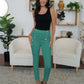 Woman wearing FAM-FAM high waist skinny pants in green with decorative buttons, styled with a black top in a modern living room setting.