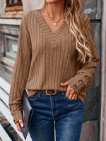 Woman wearing ribbed V-neck long sleeve t-shirt with decorative buttons, paired with jeans and holding a clutch.