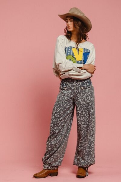 Model wearing a cozy sweatshirt with colorful graphic and flowy printed pants against a pink background.