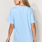 Woman wearing light blue graphic round neck short sleeve T-shirt, rear view, paired with blue jeans.