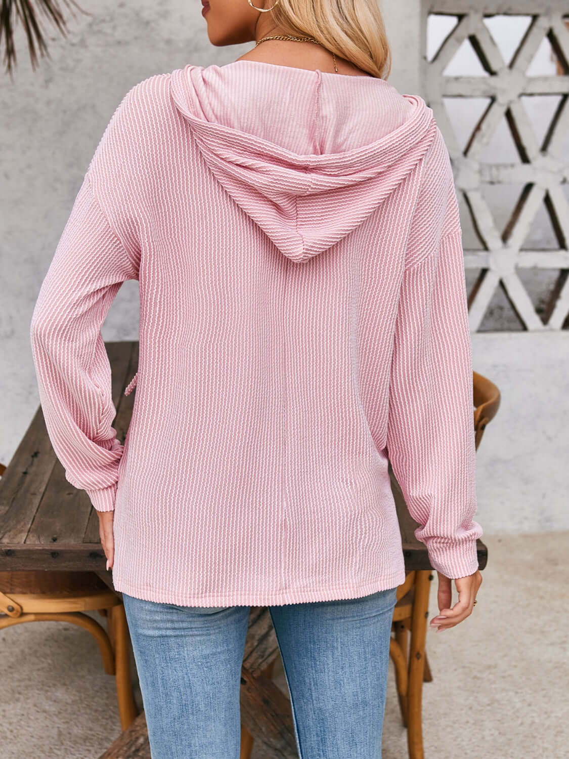 Woman wearing pink drawstring dropped shoulder long sleeve hoodie, shown from the back.