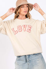 Woman wearing LOVE Path Applique Drop Shoulder Sweatshirt with relaxed fit and red LOVE patch, paired with jeans.