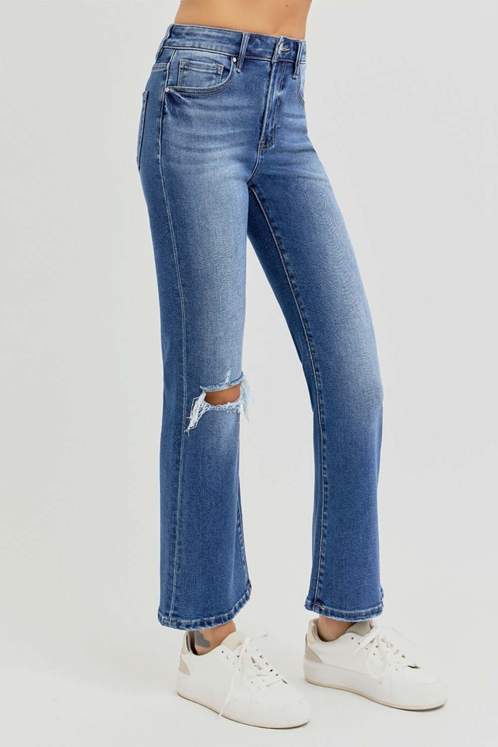 Risen distressed high rise crop flare jeans with ripped knee, paired with white sneakers for an edgy and casual look.