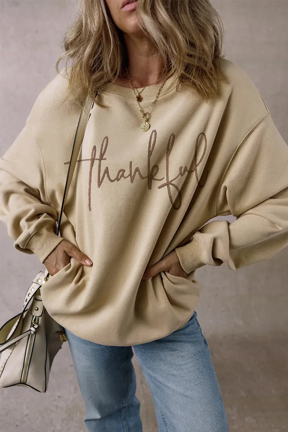 Woman wearing Bella Road Thankful Round Neck Long Sleeve Sweatshirt with jeans and a handbag