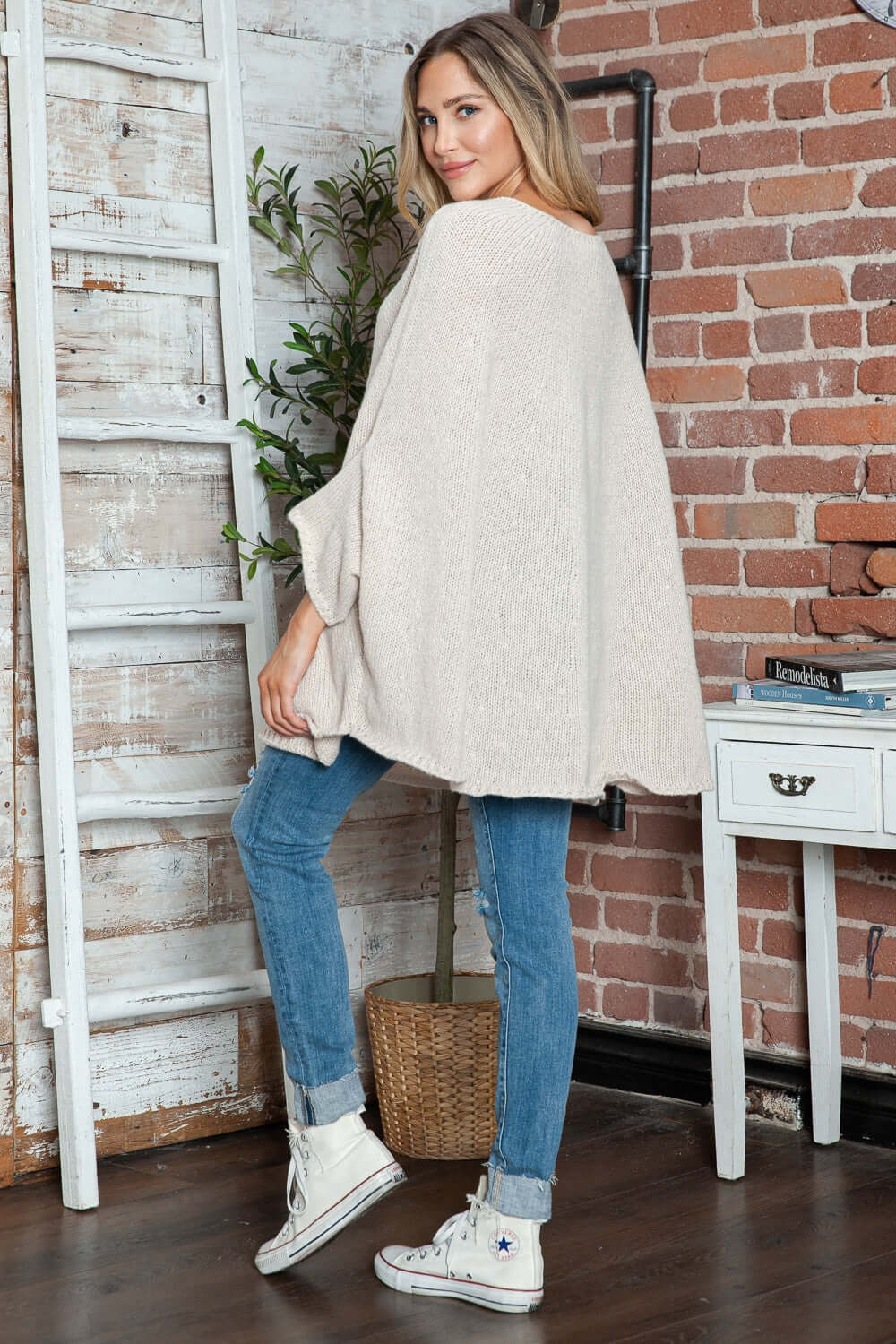 Woman wearing Bella Road Round Neck Batwing Sleeve Sweater, posing indoors with casual jeans and sneakers for a stylish look.