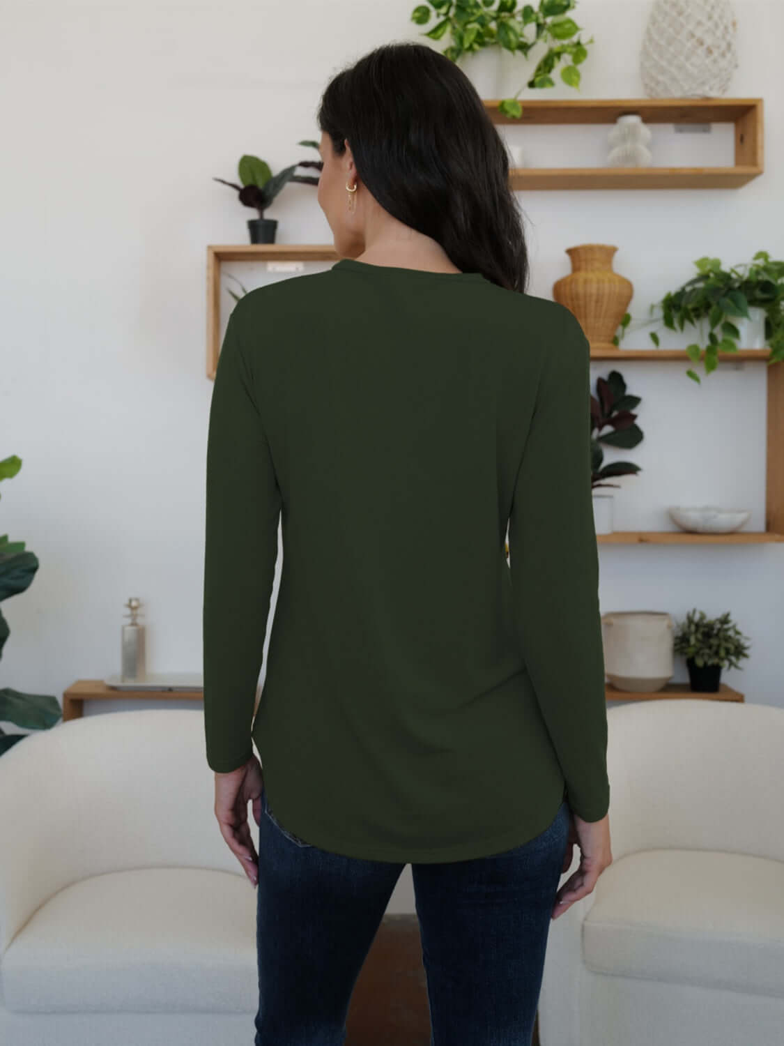 Woman wearing FAM-FAM round neck long sleeve t-shirt in army green, showcasing stylish back view in a cozy room setting.