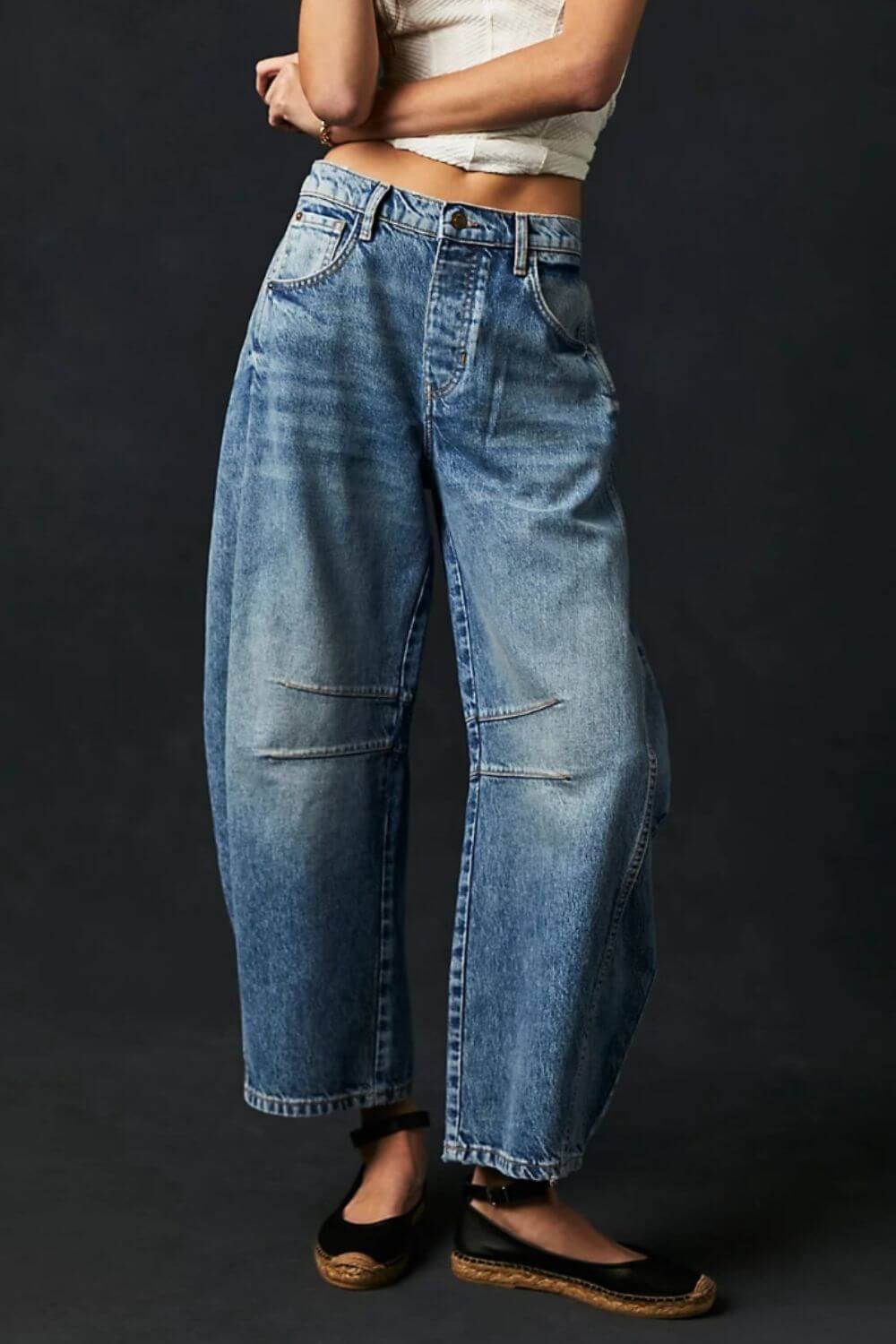 Wide leg jeans with pockets in blue denim, featuring button closure and no stretch, worn by model with black flats against dark background