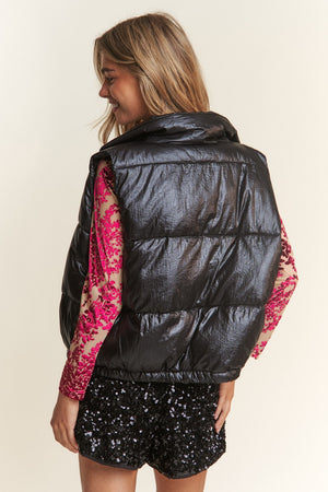 Woman wearing J.NNA snap and zipper shiny metallic puffer vest, styled with a sequin outfit for a chic look.