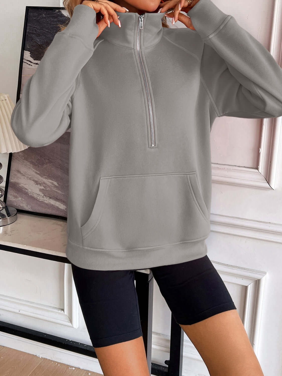 Ivy Lane Half Zip Raglan Sleeve Pocketed Sweatshirt in grey with black shorts, front view in indoor setting