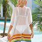 Woman wearing white slit openwork V-neck half sleeve cover-up with rainbow hem, standing by a pool with palm trees in the background.