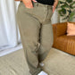 Woman wearing RFM Full Size High Rise Garment Dye Wide Leg Jeans in olive green standing in a stylish living room.