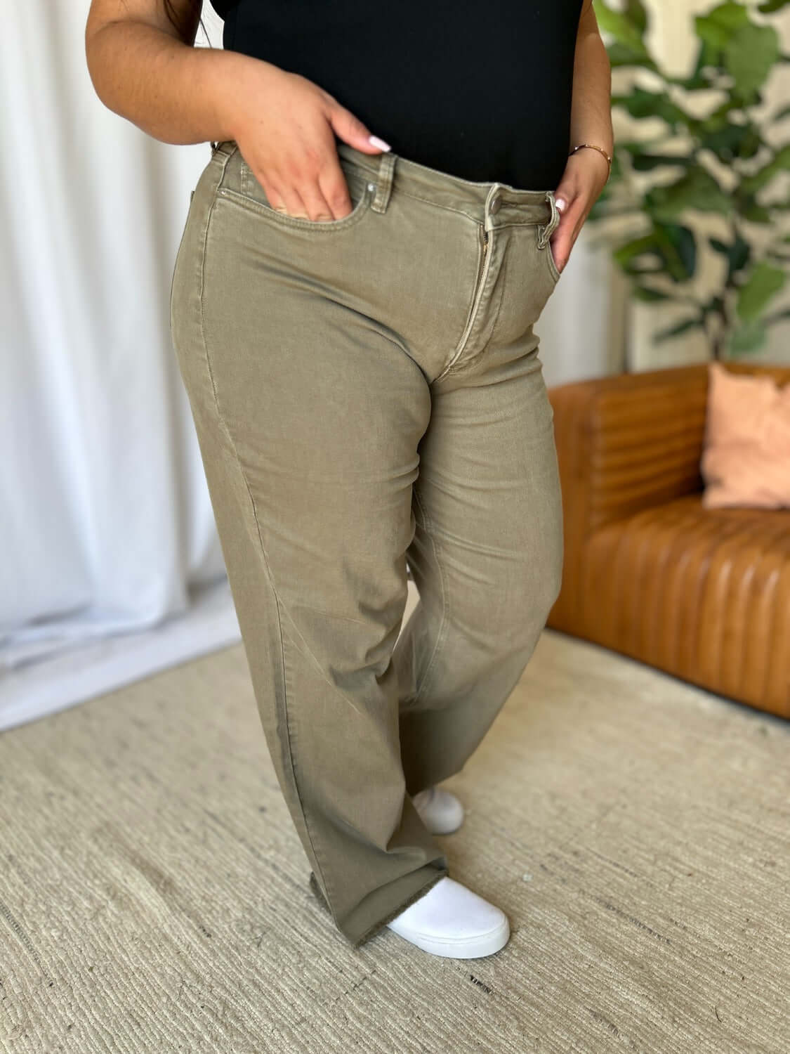 Woman wearing RFM Full Size High Rise Garment Dye Wide Leg Jeans in olive green standing in a stylish living room.