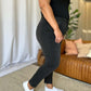 Woman wearing RFM Full Size High Rise Tummy Control Skinny Jeans in dark color, standing indoors near a sofa.