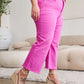 Woman wearing Crop Chloe Full Size Tummy Control High Waist Raw Hem Jeans in pink, paired with white top and wedge sandals