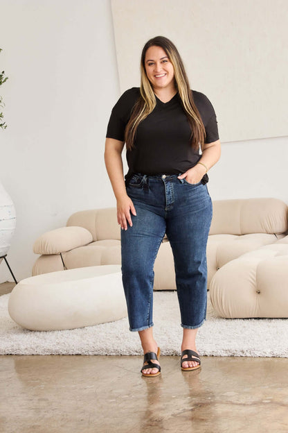 Woman wearing Tummy Control High Waist Raw Hem Jeans from RFM Jeans, standing in stylish living room setting.