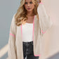 Chic woman in beige open front cardigan with pink accents, showcasing trendy Double Take Contrast style against a soft background.