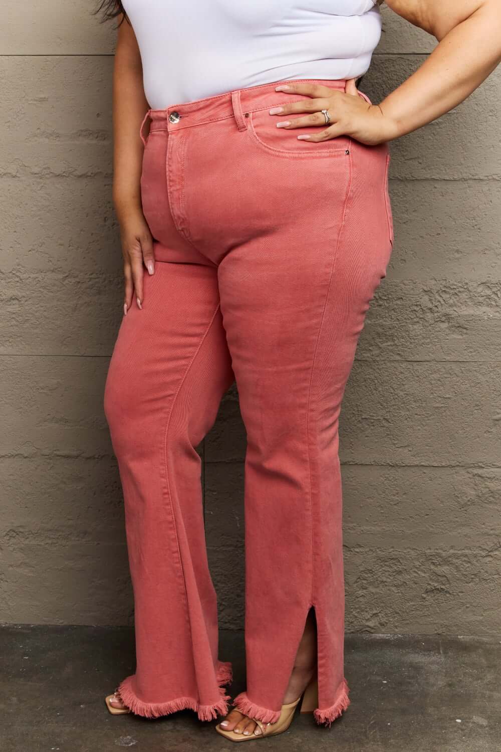 Woman wearing Bailey High Waist Side Slit Flare Jeans in pink, showcasing side slit detail and frayed hems from Risen Jeans.