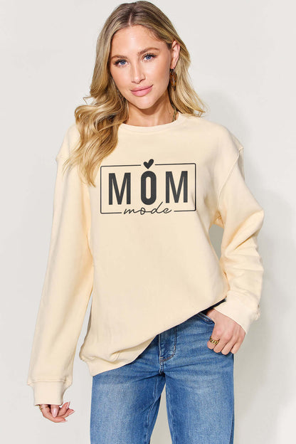 Woman wearing a letter graphic long sleeve "MOM mode" sweatshirt in beige paired with blue jeans.