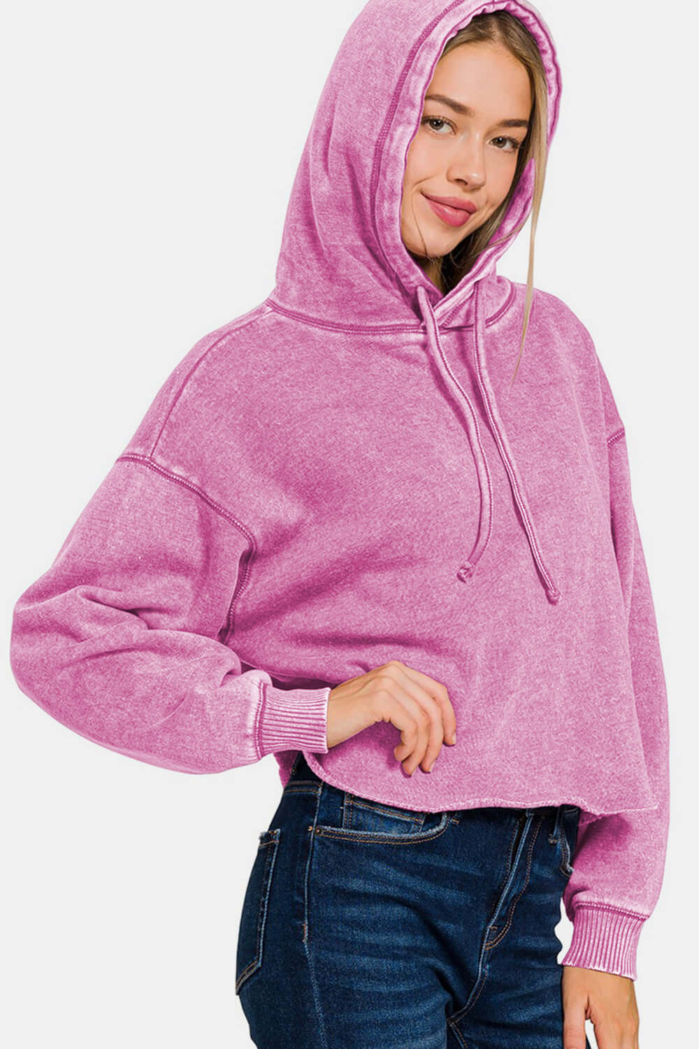 Woman wearing a Zenana Acid Wash Fleece Cropped Hoodie in pink, showcasing its trendy and edgy style with a cozy fleece fabric.