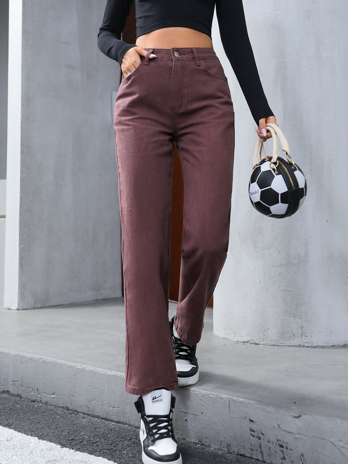 Stylish woman in dark brown denim straight leg jeans, holding a soccer ball handbag, ready for a casual outing.