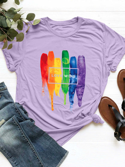 Lavender graphic round neck short sleeve t-shirt with 'Love Wins' rainbow paint design, paired with denim jeans and sandals.