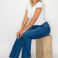 Woman in high rise straight jeans sitting on a wooden block, showcasing a stylish casual look with a classic white tee.