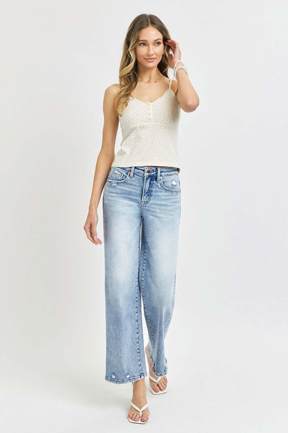 Woman wearing RISEN Full Size Tummy Control High Rise Crop Wide Leg Jeans in light wash with a white top and sandals