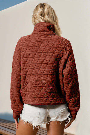 Woman wearing quilted half zip long sleeve sweatshirt with pocket in rust color, featuring stylish diamond pattern design.