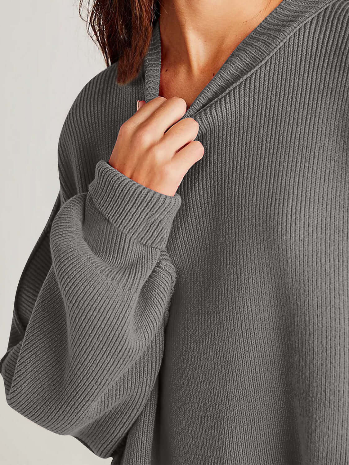 Woman wearing a cozy side slit round neck long sleeve sweater in a grey ribbed knit.