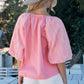 Woman wearing pink poplin bubble sleeve blouse and white shorts, standing outdoors with straw hat