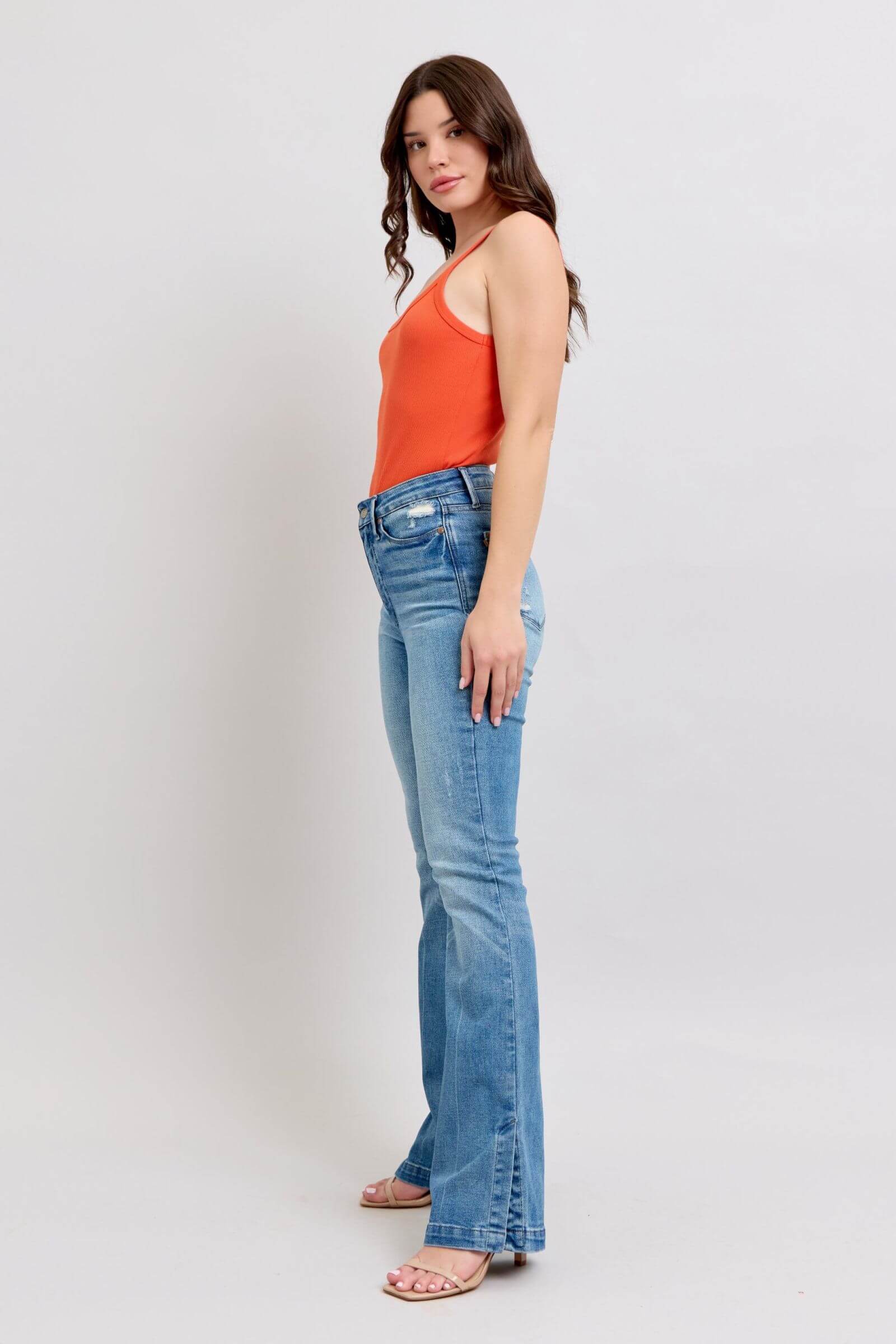 Model wearing Judy Blue high waist jeans with tummy control, featuring a vintage wash and side slit, styled with an orange top.